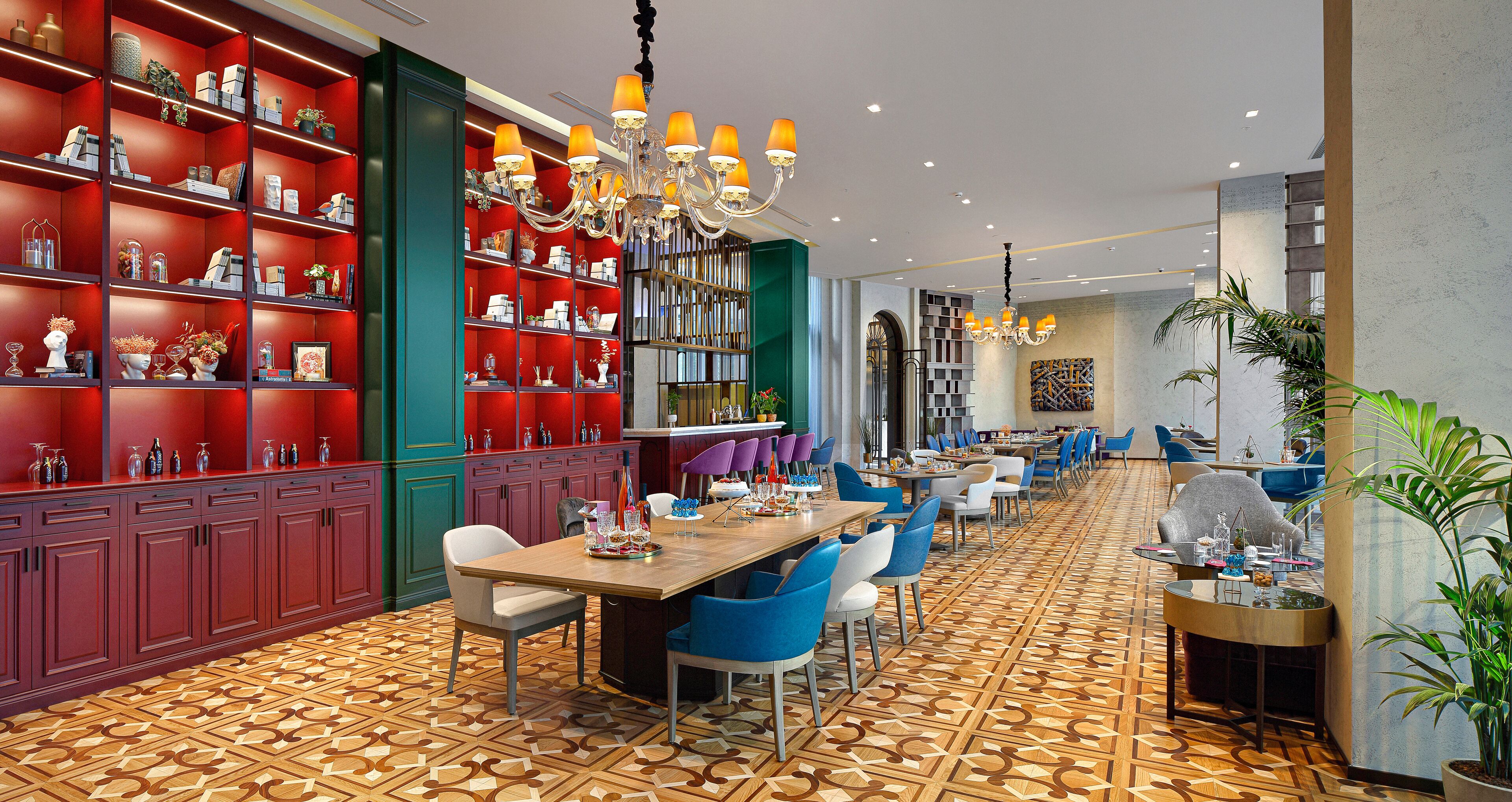 A spacious dining area with a long wooden table, blue and white chairs, and a red bookshelf filled with decorative items.