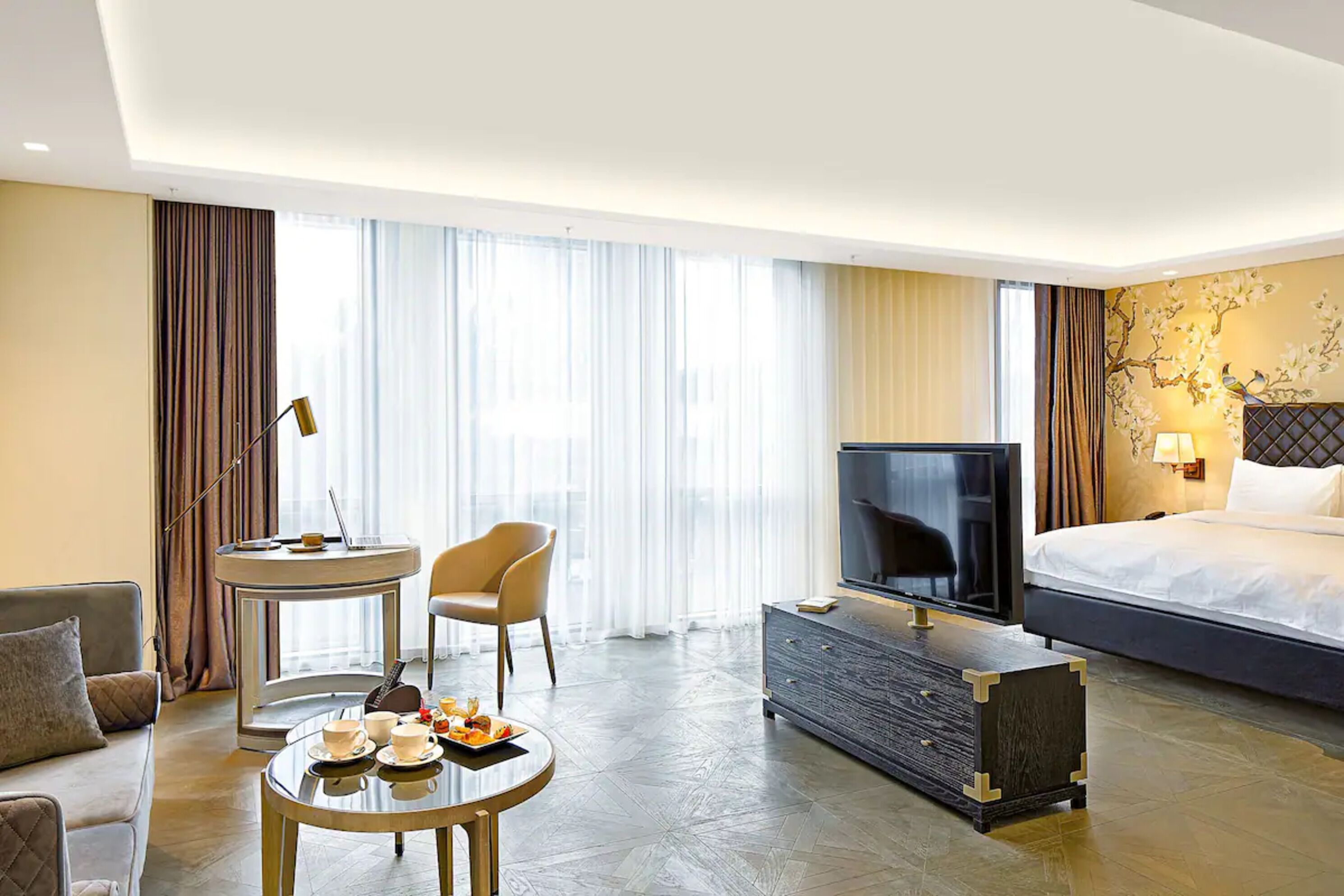 A hotel room with a bed, a TV, a dining table with a chair, a sofa, and a small side table.
