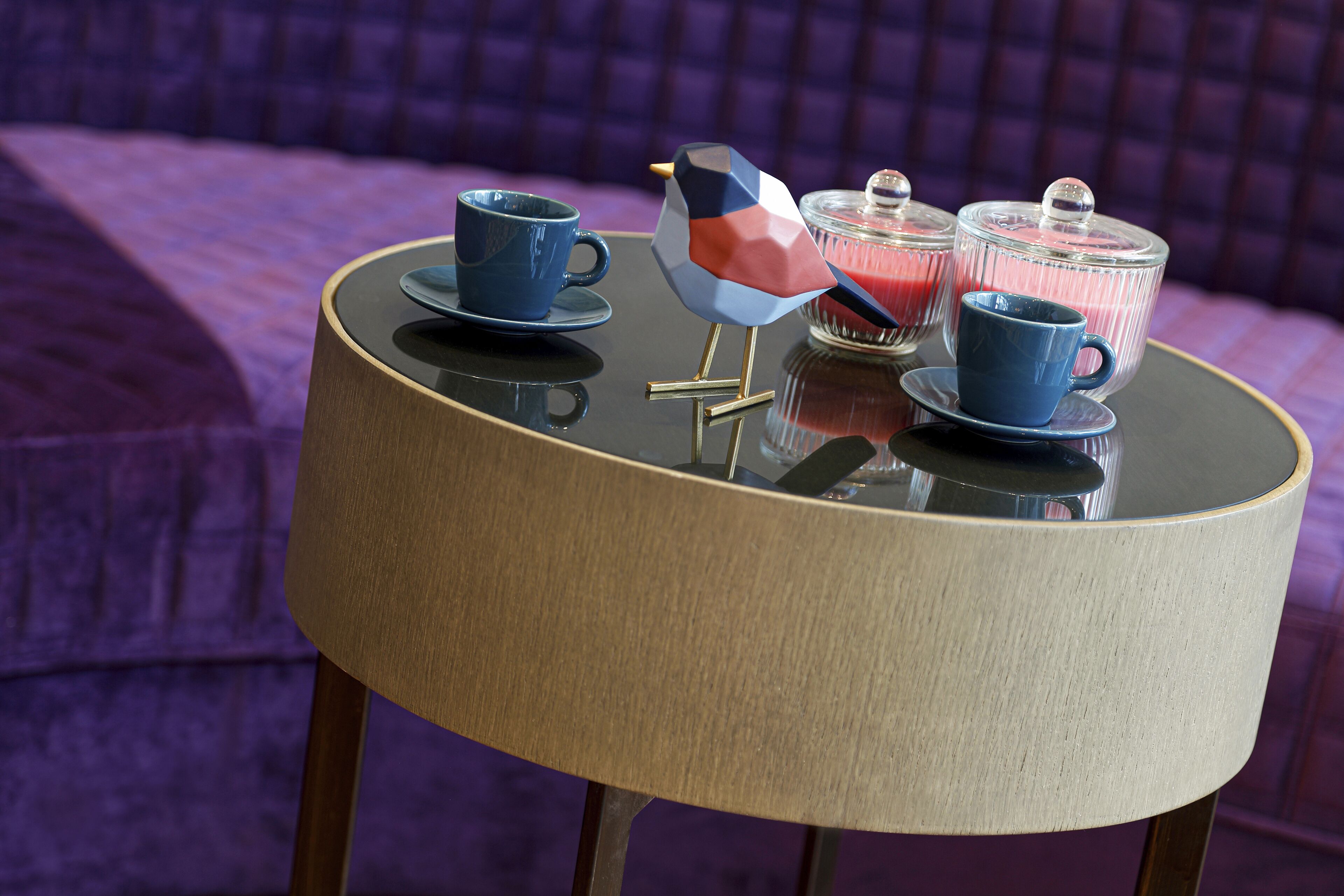 Une table ronde avec une tasse bleue, un objet en forme d’oiseau et un récipient en verre doté d’un couvercle.