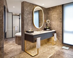 Ein modernes Badezimmer mit Marmorboden, einem großen Spiegel mit Goldrahmen, einem Waschbecken und einem Waschtisch mit Handtuchhalter.
