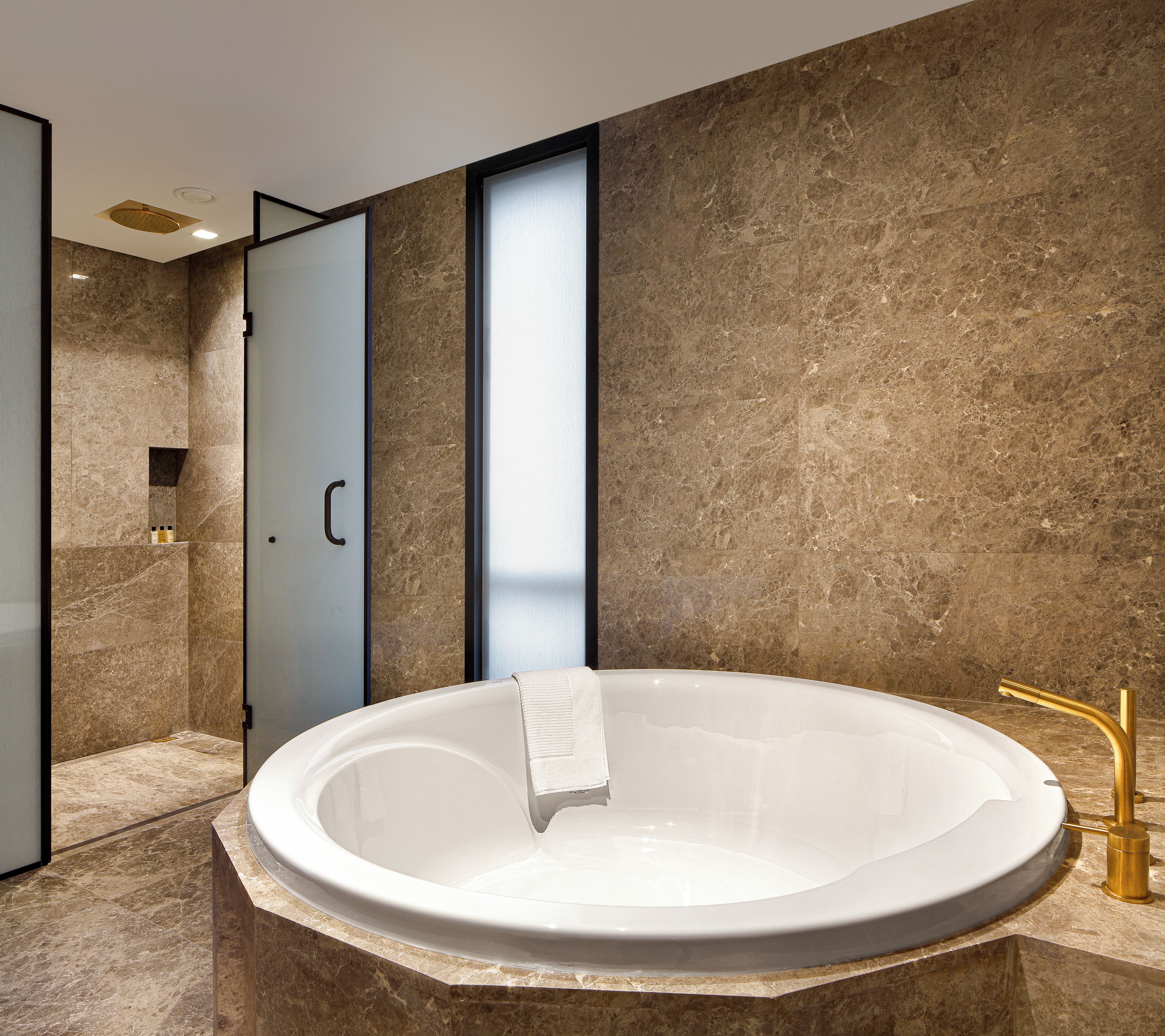 A modern bathroom with a freestanding bathtub, marble walls, and a gold faucet.