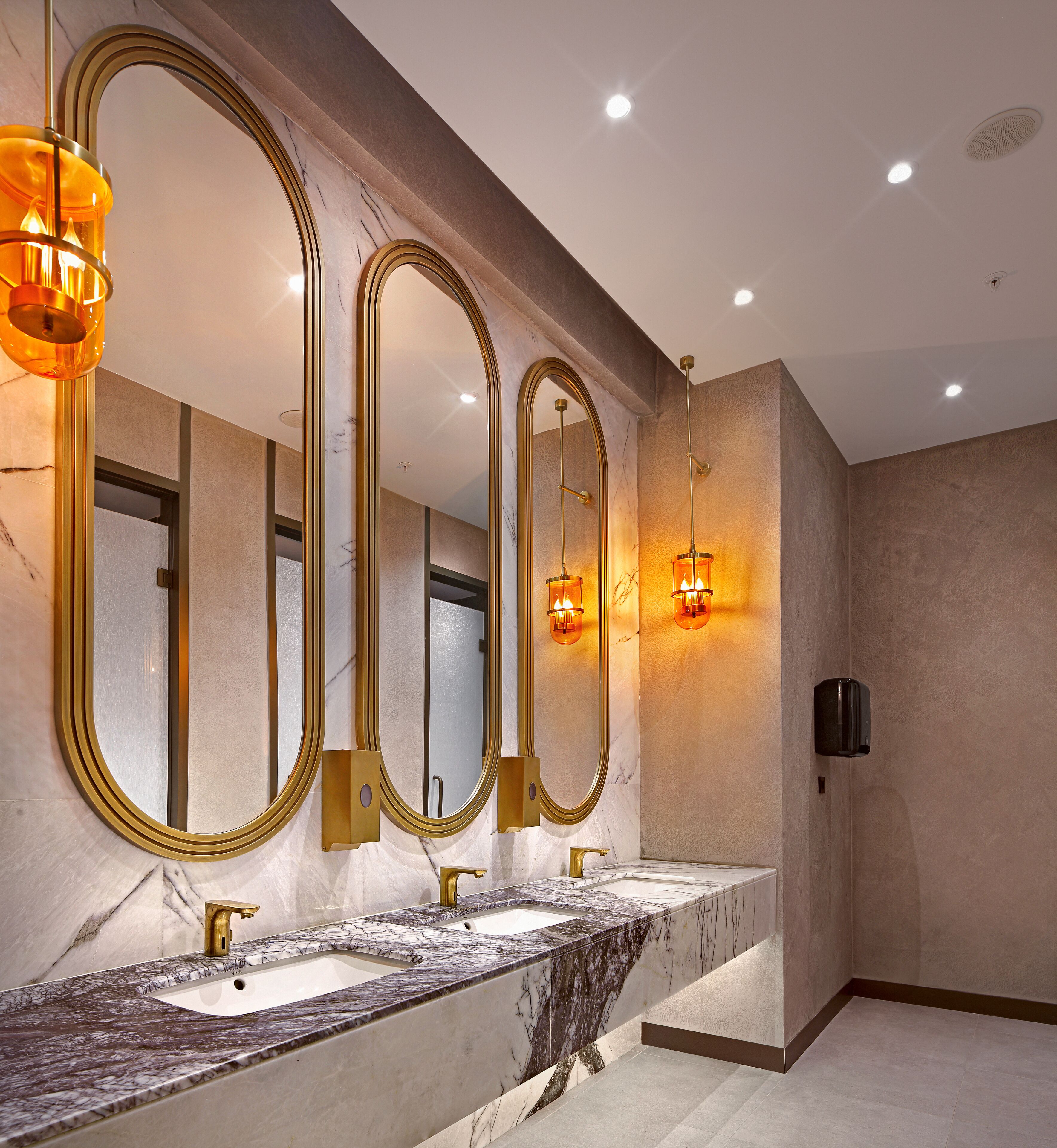 A bathroom with three mirrors, a marble countertop, and a gold faucet.