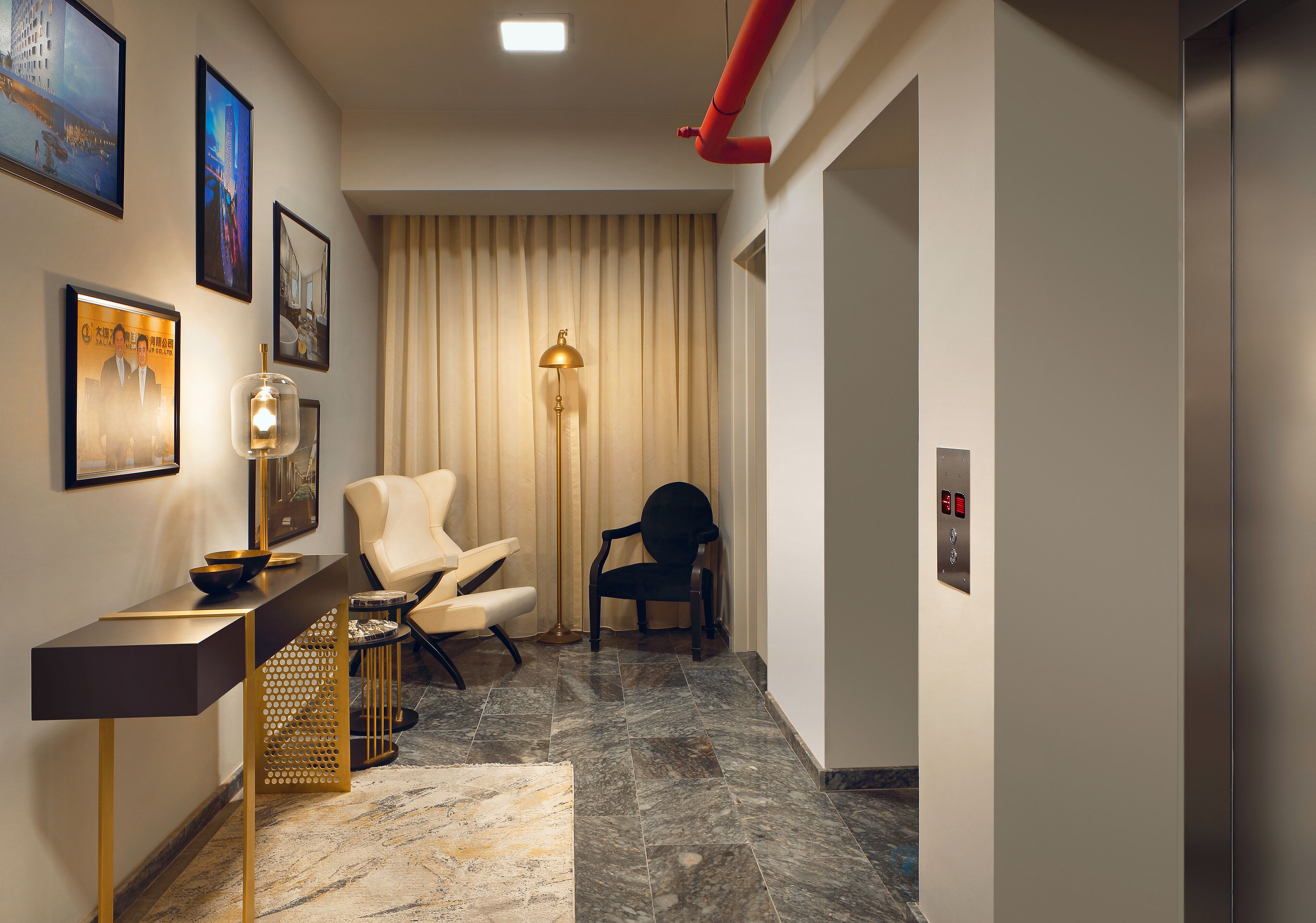 A modern hotel lobby with a reception desk, two chairs, a floor lamp, and a large window with curtains.