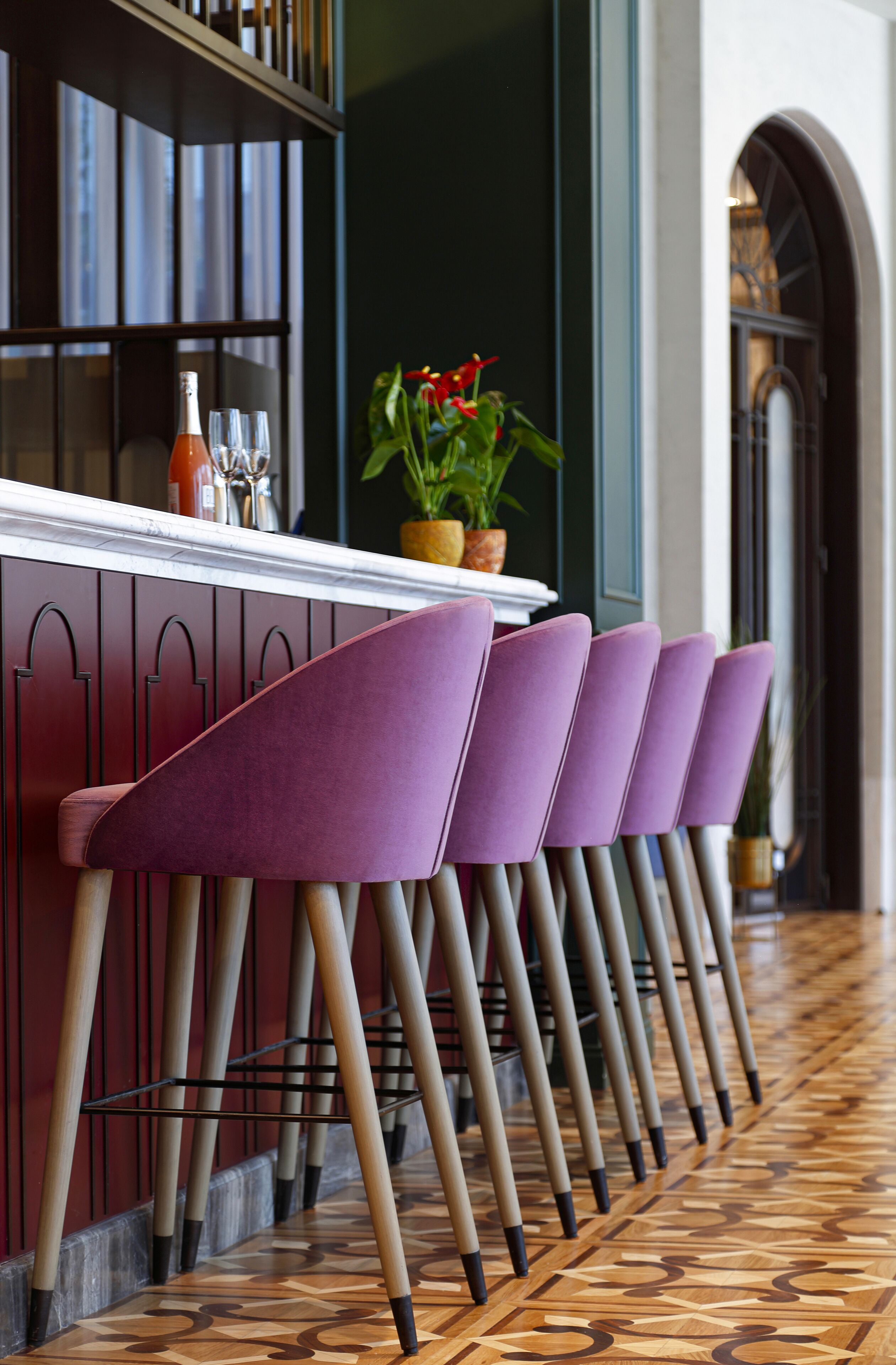 A row of purple chairs with wooden legs and a bar area with a bottle and glasses.