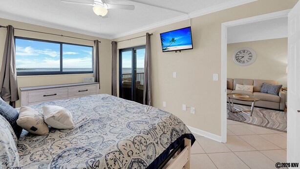 Une chambre à coucher avec un lit, un ventilateur de plafond, une télévision, une horloge et une vue sur l’océan.