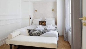 A neatly arranged bedroom with a large bed, a bench, and a window with curtains. - A Dazzling 2-BR apartment in Le Marais (Paris)