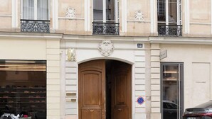 A building with a large wooden door, a shop on the ground floor, and a car parked outside. - A Dazzling 2-BR apartment in Le Marais (Paris)