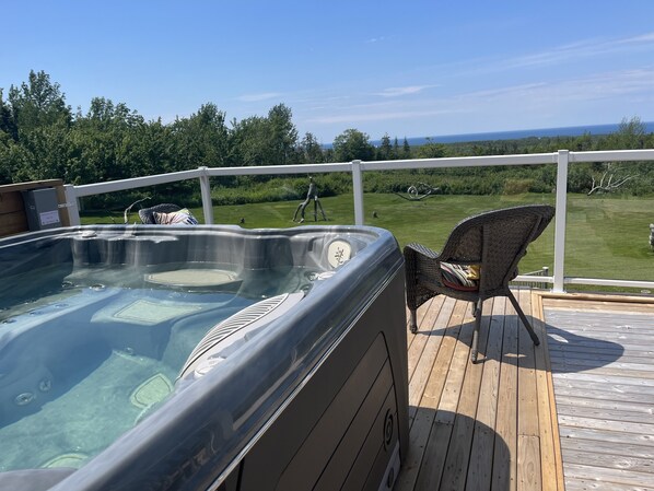 Un bain à remous sur une terrasse en bois, avec vue sur une zone herbeuse et des arbres.