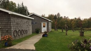 A wooden cabin with a 'STUDIO' sign, a gravel path leading to the door, and a well-maintained lawn with trees and shrubs. - Doug Fraser Artist Loft Suite (Inverness)