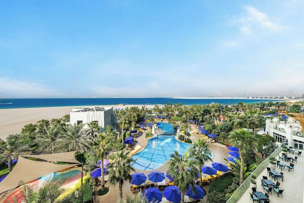 A resort with a swimming pool, palm trees, and a beach view.