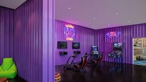 Ein Gaming-Bereich in Lila mit Neon-Schildern, Gaming-Stühlen und mehreren Spielstationen.