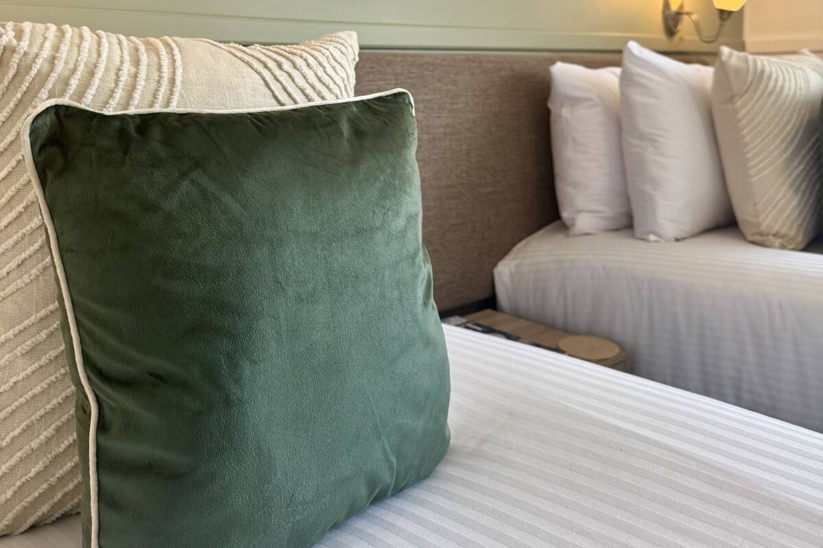 Ein Hotelzimmer mit einem Bett, Kissen, einer Wandlampe und gerahmten Pflanzenbildern.
