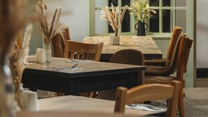 A dining area with a wooden table, chairs, and a vase with dried plants.