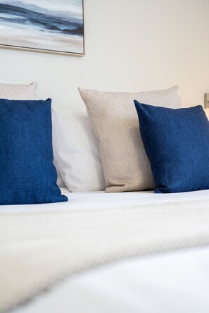 A bed with white bedding and three pillows in different colors.