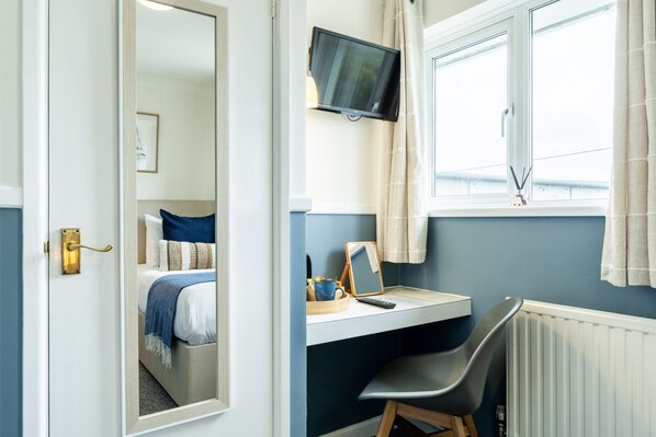 A bedroom with a bed, a desk with a computer, a television, and a window with curtains.