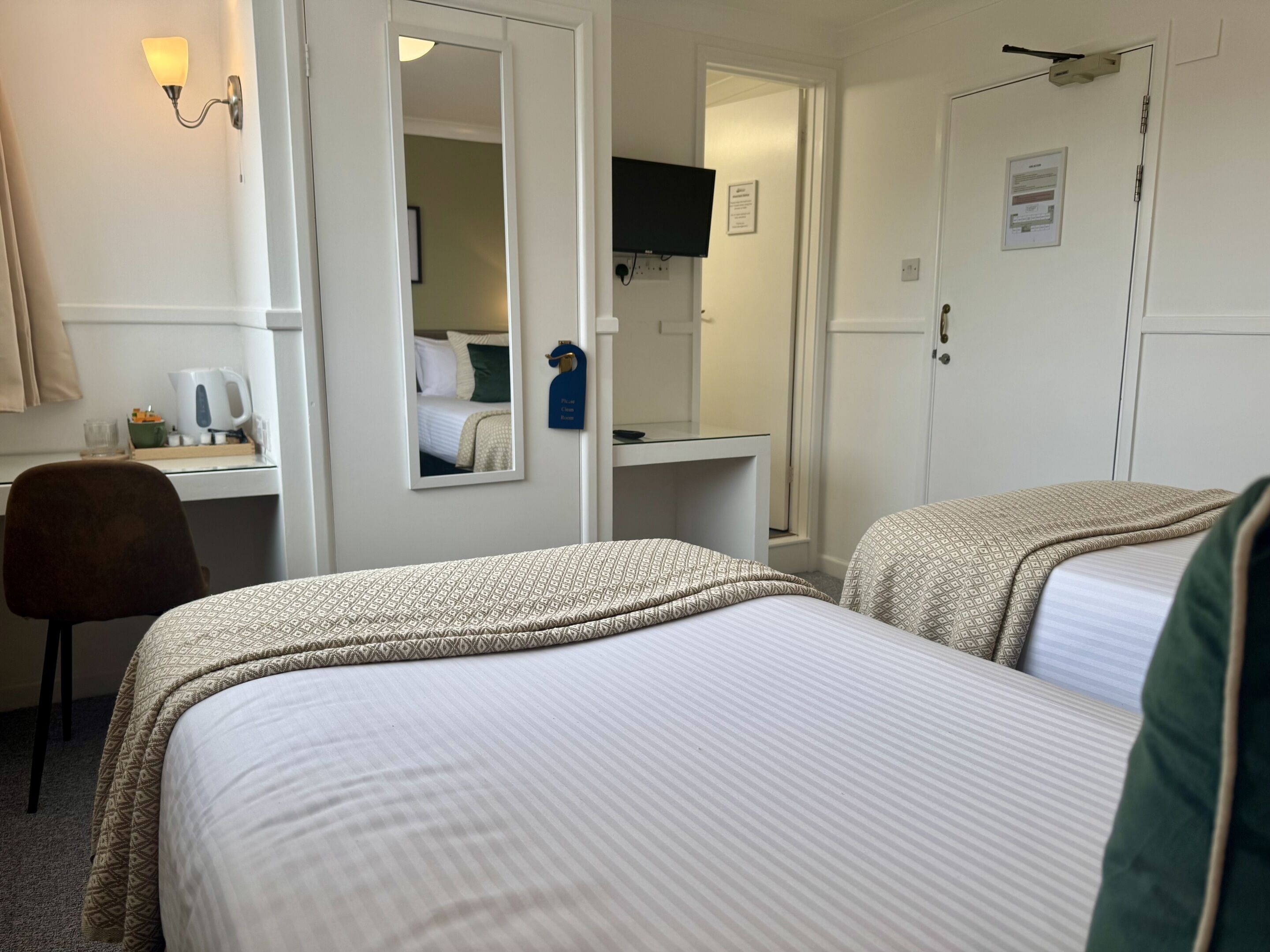 A hotel room with two beds, a desk, a chair, a mirror, and a television.