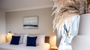 A hotel room with a bed, a nightstand, a vase with pampas grass, and a bottle of perfume.