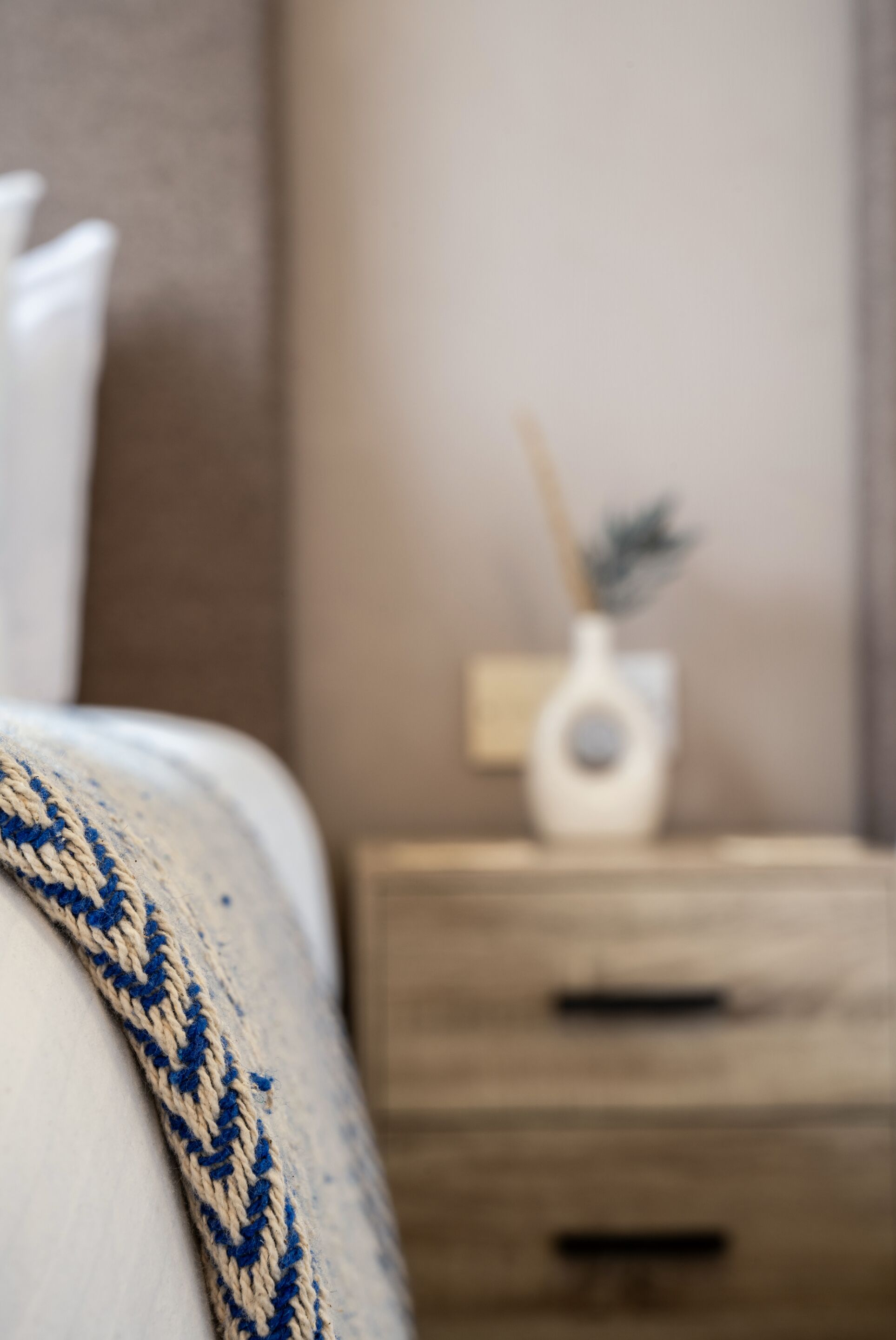 Un dormitorio con una cama, una mesita de noche con lámpara y una mesita auxiliar de madera.