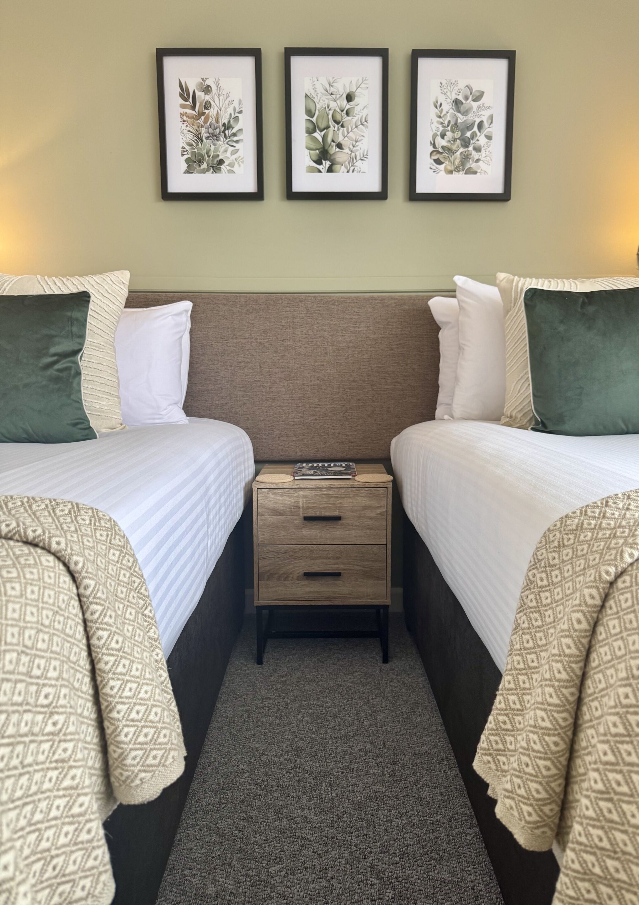 Une chambre d’hôtel avec deux lits, une table de chevet et trois reproductions botaniques encadrées accrochées au mur.