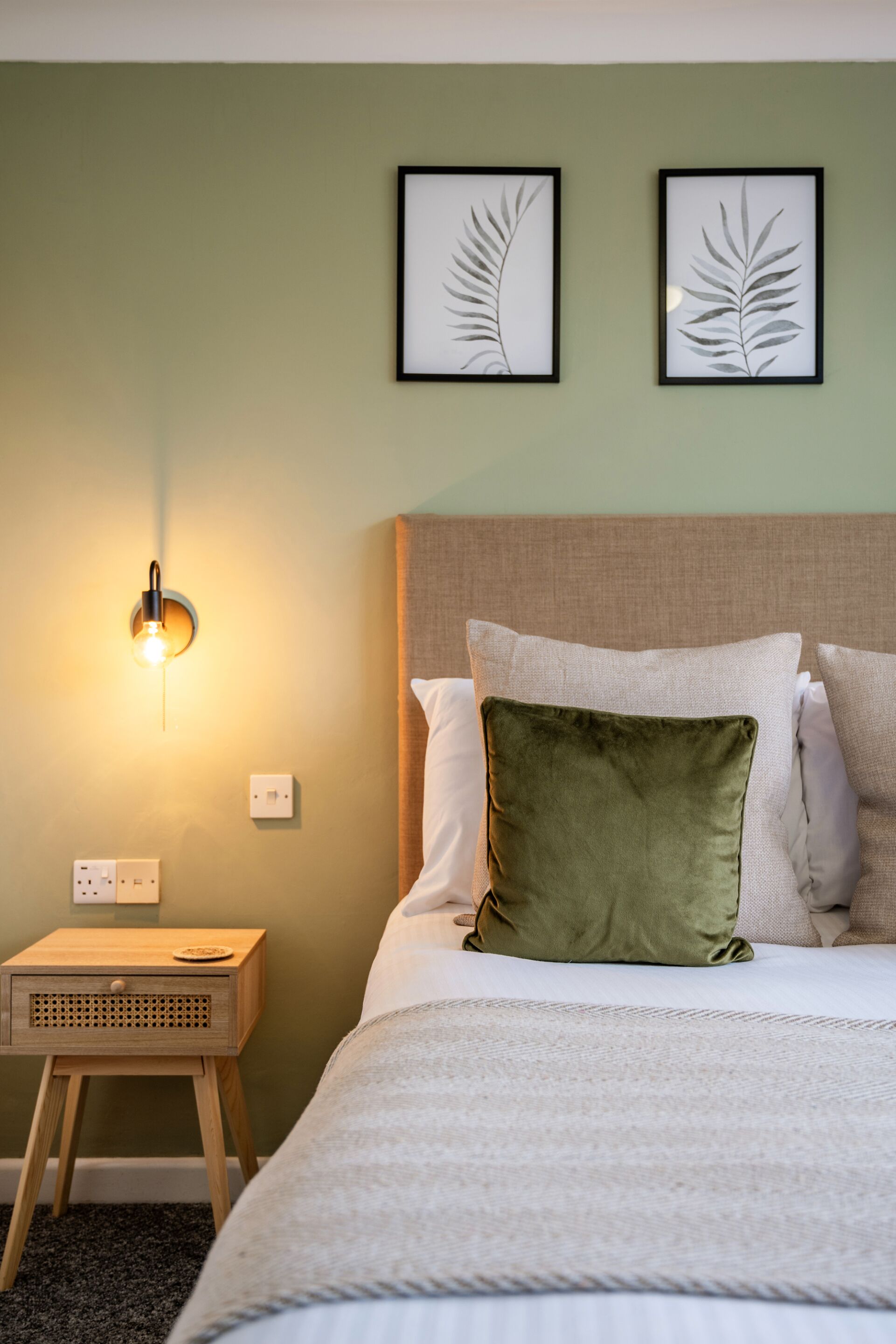 Un dormitorio ordenado con cama, mesita de noche y lámpara de pared.