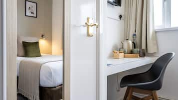 Una habitación de hotel con cama, escritorio, silla, televisor y ventana con cortinas.