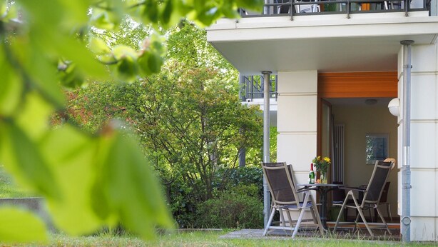 Un espace extérieur aménagé avec une table et des chaises, entouré de verdure et d’un bâtiment.