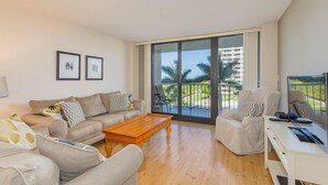 A spacious living room with a large sliding glass door leading to a balcony with a view of palm trees and buildings. - Located in the desirable Marco Island community of South Seas (Marco Island)