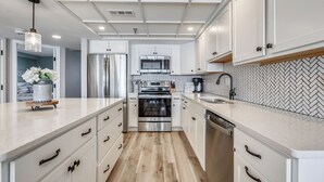 A modern kitchen with white cabinetry, stainless steel appliances, and a herringbone-patterned backsplash.