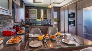 Une cuisine moderne avec un coin repas, dotée d’un pare-feu en pierre, d’appareils électroménagers en acier inoxydable et d’une table à manger en verre, prête pour le petit-déjeuner.