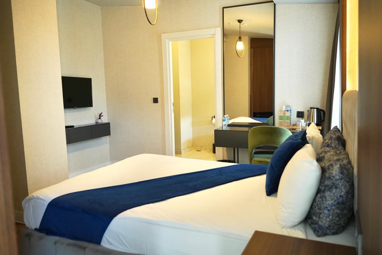 Una habitación de hotel con cama, escritorio, silla, televisor y espejo.
