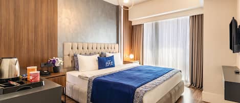 A modern hotel room with a large bed, a bedside table with a lamp, a flat-screen TV, and a wooden floor.