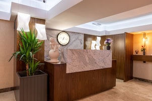 A hotel reception desk with a marble top, a clock, and a potted plant.