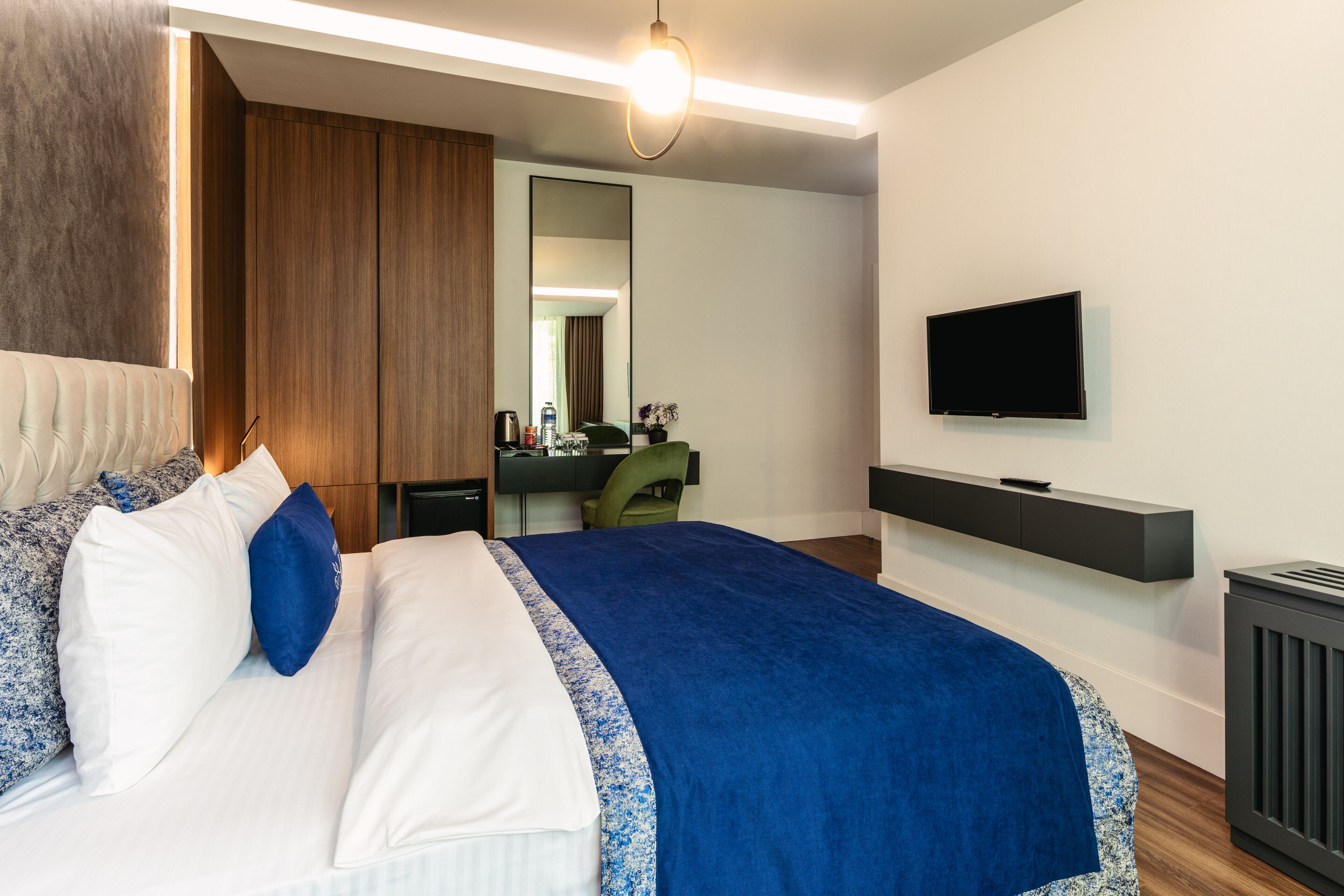Et moderne hotelværelse med en stor seng, et fjernsyn monteret på væggen og et skrivebord med stol.