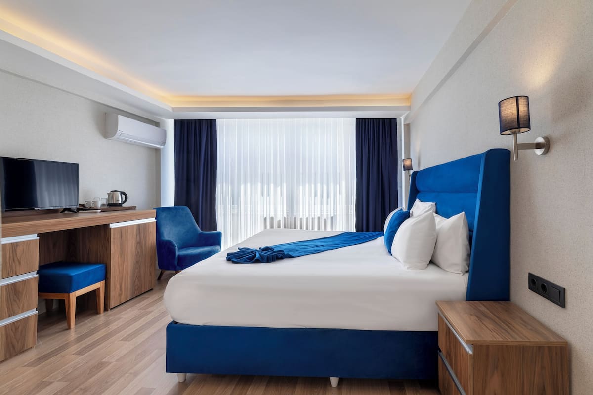 Ein modernes Hotelzimmer mit einem großen Bett, einem Schreibtisch, einem Sessel und einem Fernseher.