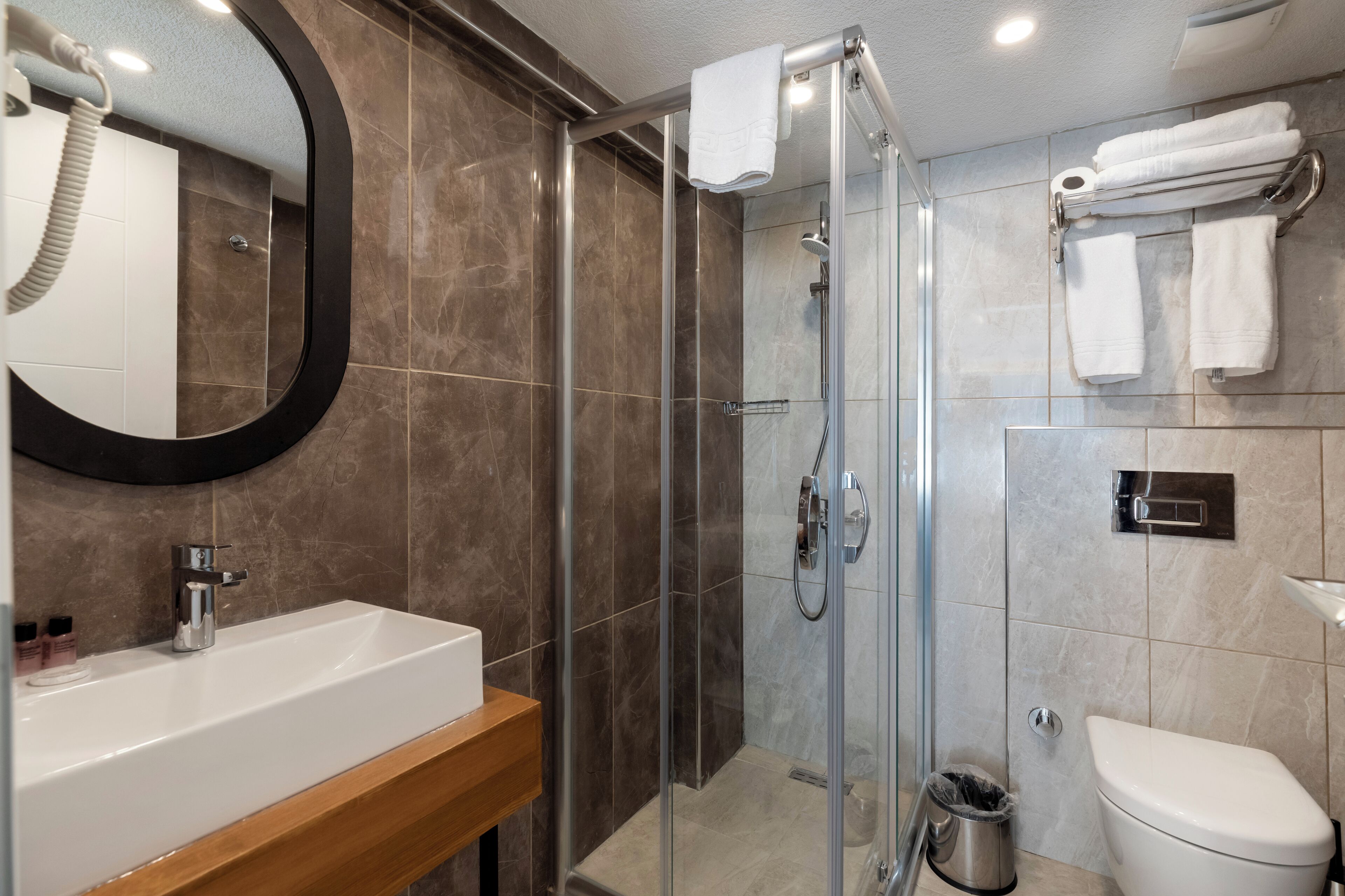 A modern bathroom with a glass-enclosed shower, a white sink with a wooden countertop, and a toilet.