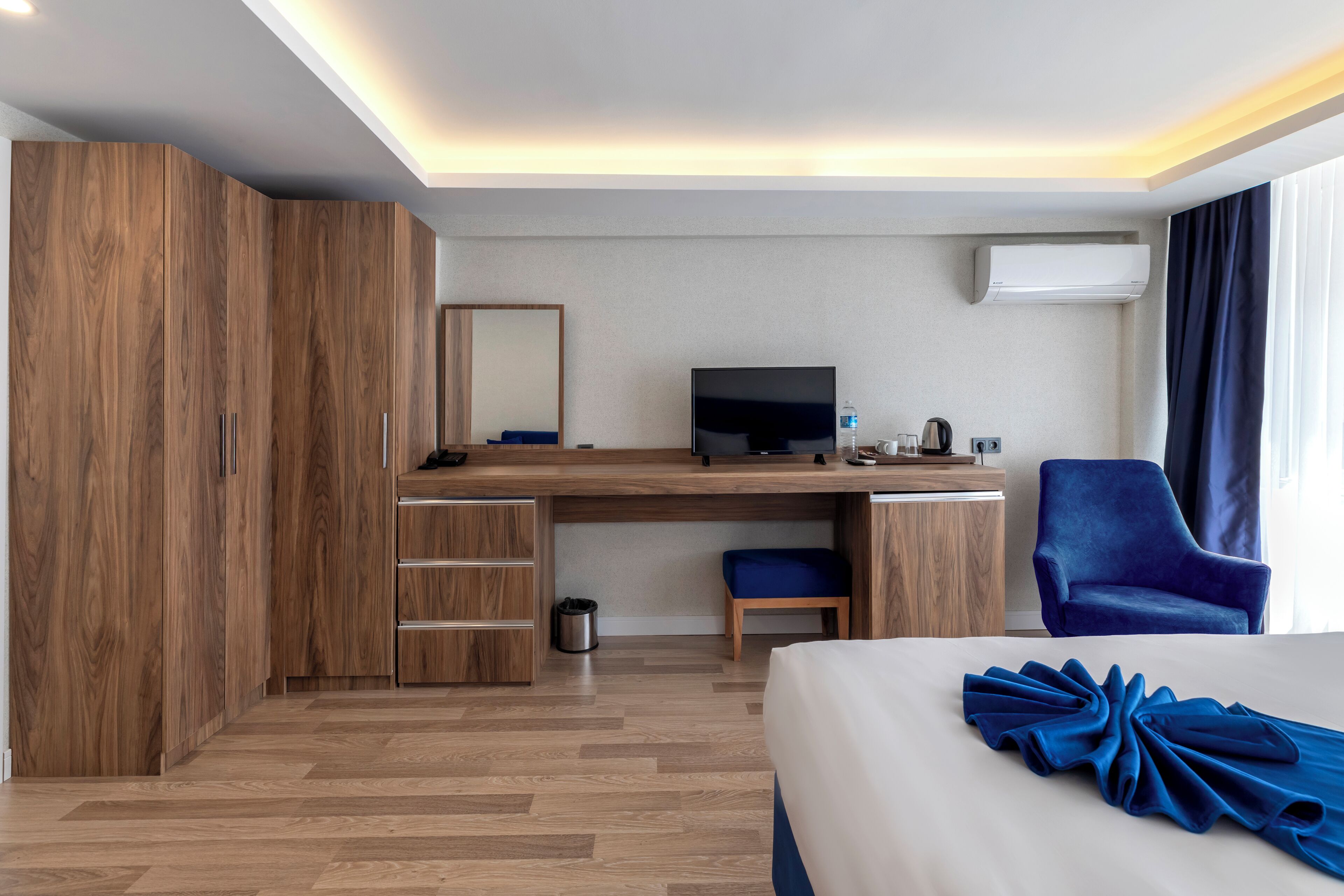 Een hotelkamer met een houten bureau, een televisie, een stoel, een bed en een grote garderobe.