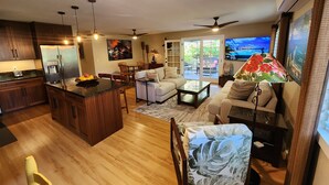 A modern kitchen with a central island, dining area with chairs, a sofa, and a TV.