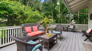 A covered outdoor deck with wicker furniture, a table, and a potted plant.