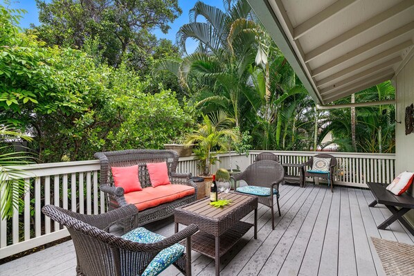 A covered outdoor deck with wicker furniture, a table, and a potted plant.