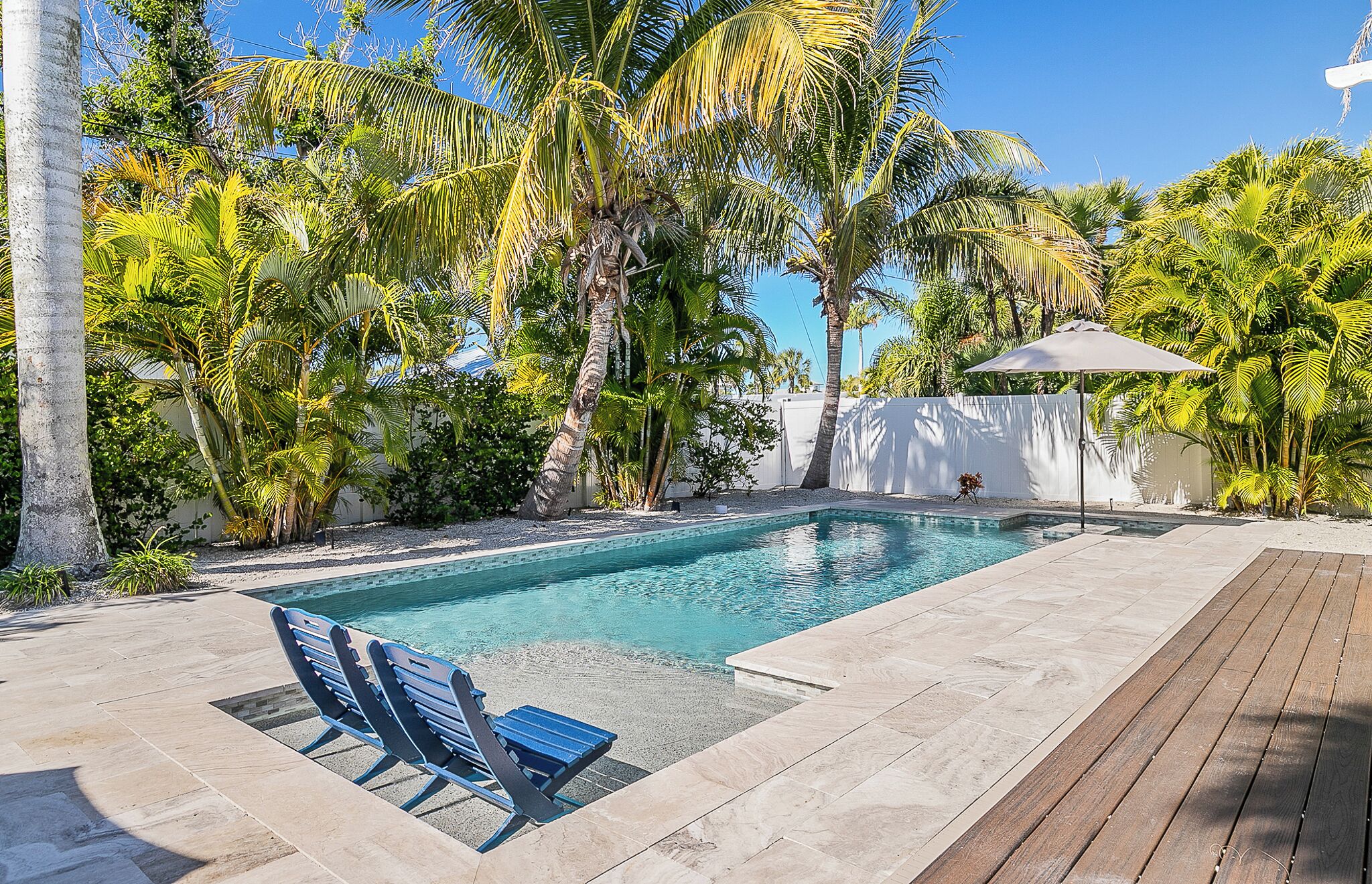 A swimming pool with clear blue water, surrounded by palm trees and a wooden deck.