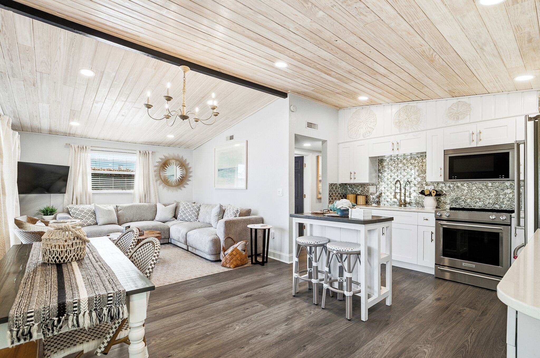 A modern kitchen with white cabinets, a central island with stools, a built-in oven, and a stainless steel refrigerator.
