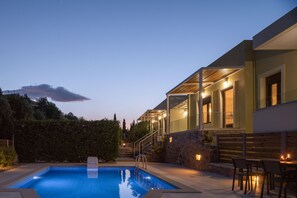 A modern pool area with a clear blue pool, stone steps leading to a covered outdoor area, and a seating arrangement with tables and chairs.