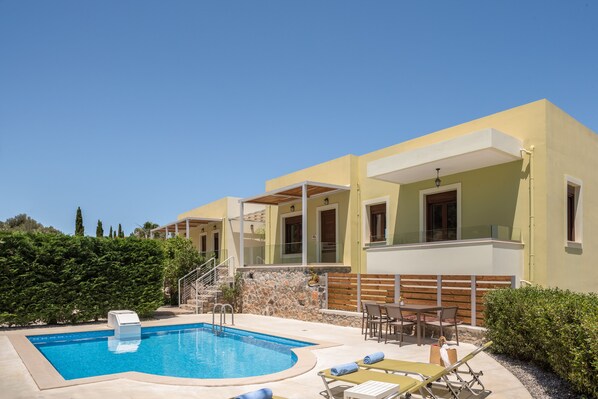 A modern hotel with a swimming pool, outdoor seating, and a stone wall.