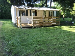 En liten träbyggnad med en veranda, vita plaststolar och ett bord.