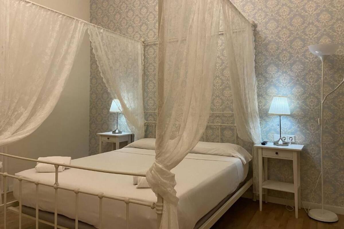 A bedroom with a four-poster bed, two bedside tables, and a floor lamp.