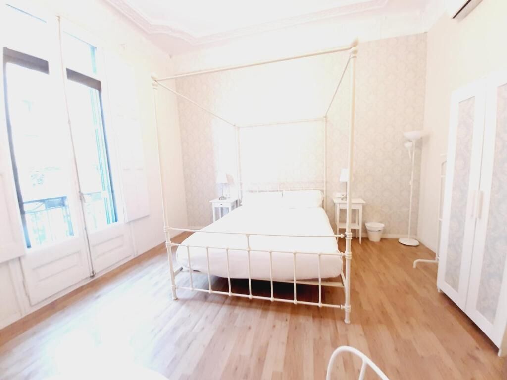 A room with a metal bed frame, a bedside table, a small stool, and a cabinet.