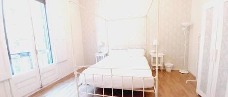 A room with a metal bed frame, a bedside table, a small stool, and a cabinet.
