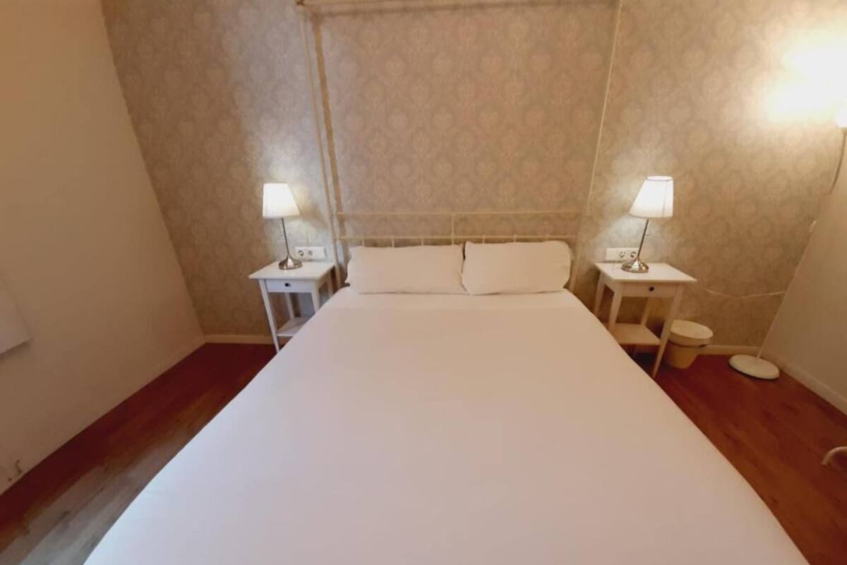 A neatly made bed with white linens in a room with patterned wallpaper and two bedside lamps.