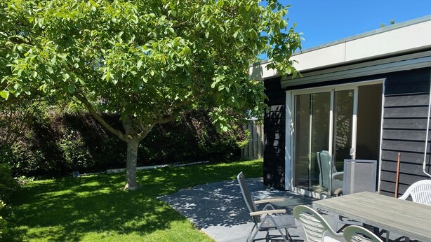 A modern outdoor patio with a table and chairs, a tree, and a building with large windows. - Quiet recreation house in Zeeland with Netflix 2 (Bruinisse)
