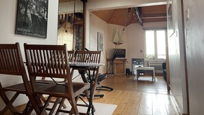 A spacious room with wooden flooring, a dining area with a table and chairs, a large window with a view, and a staircase leading to an upper level. - Appartement - 35 m2 (Saint-Malo)